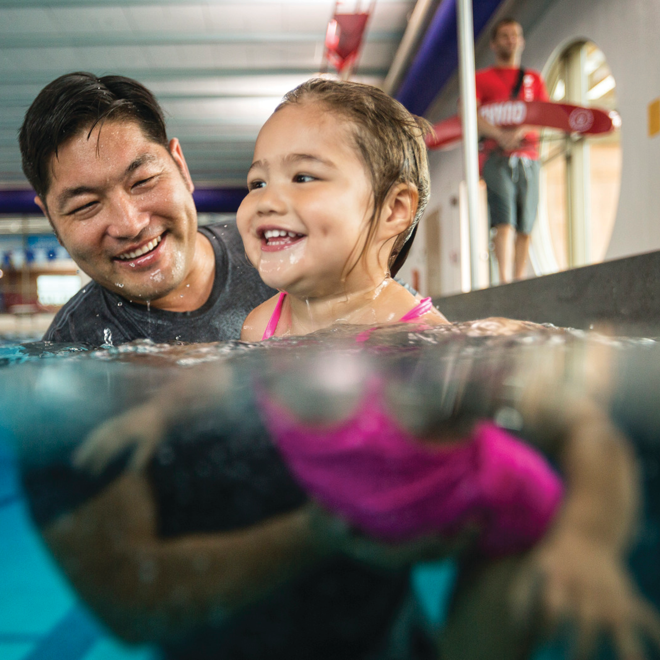 Asian father and daughter swimming together in a pool. Father is assisting daughter in a parent child swim lesson class