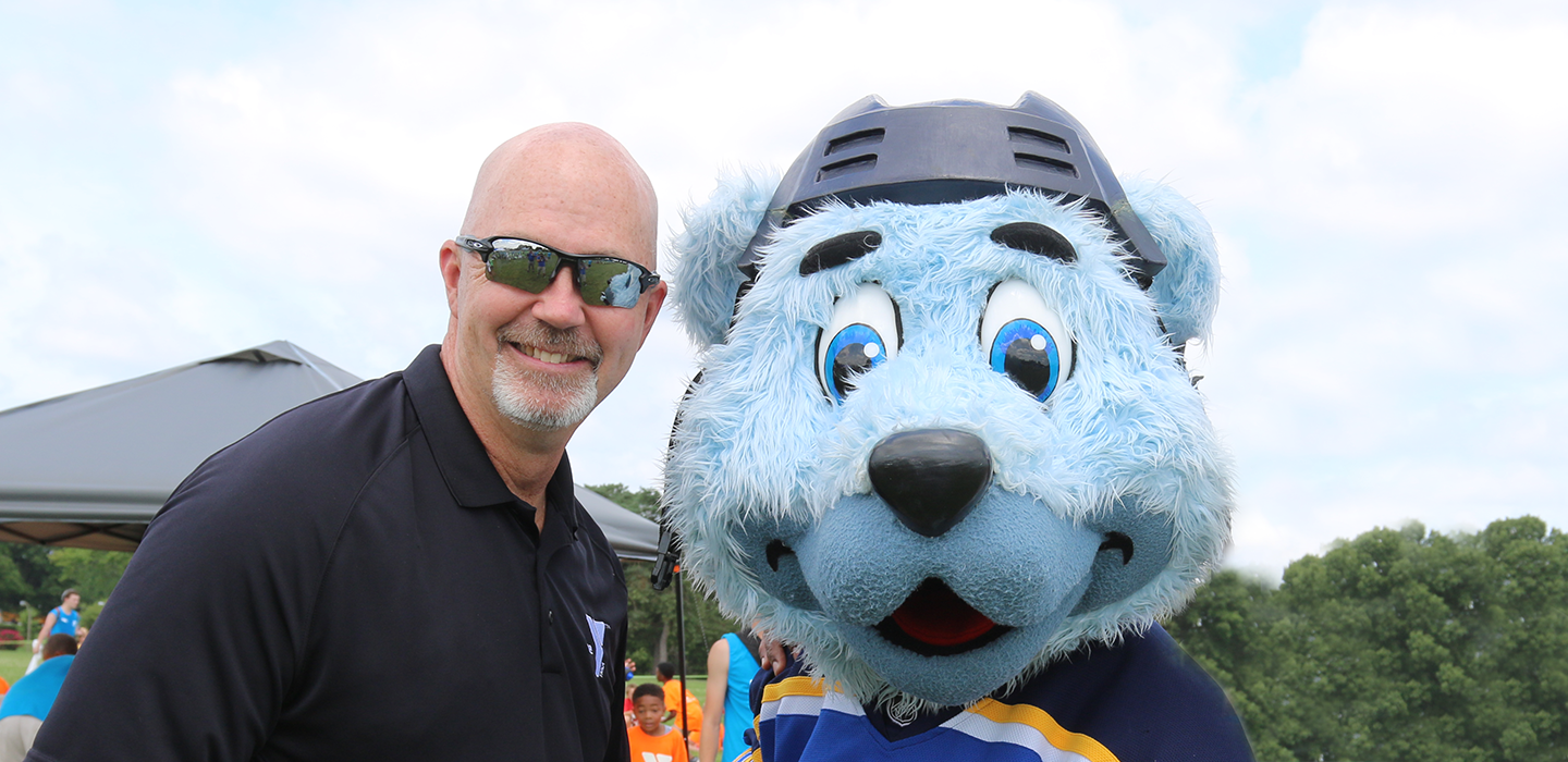 a volunteer poses with the blues mascot at a ymca summer day camp games event