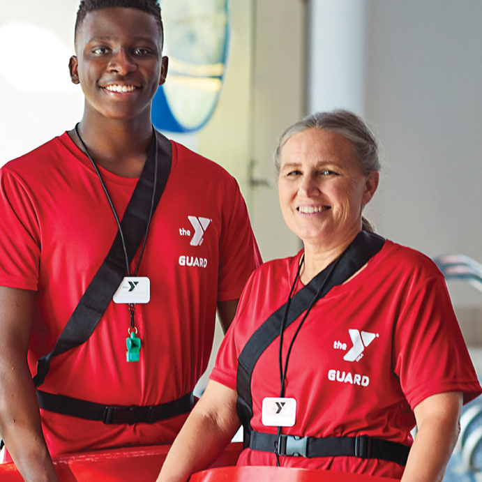 younger African American male and an older white female both wearing red YMCA shirts with a Y logo and the word guard on the shirt. 