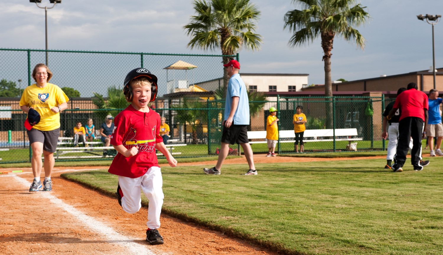A young boy in a Cardinals jersey plays baseball on Miracle league field.