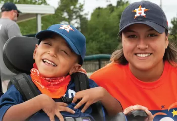 YMCA adaptive sports participant in a wheelchair smiles with his coach buddy