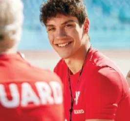 A ymca lifeguard sitting by an outdoor pool smiling 