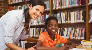 An image of a young African American boy being tutored in his reading skills during the YMCA Read program by a Caucasian female volunteer.