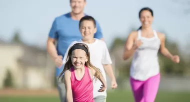 An image of a Caucasian family consisting of a young girl, teenage boy, and a mom and dad captured on a family run on a sunny day on the outdoor track of their local YMCA.