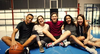 A group of teens sitting in a ymca basketball gym