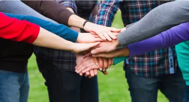 A zoomed-in image of a group of YMCA teen members putting their hands in the middle of a circle during a group huddle. 