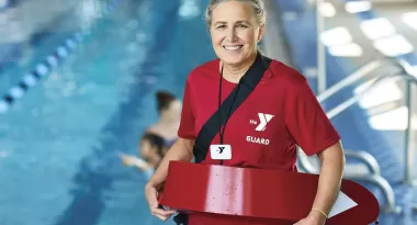 A ymca lifeguard smiling by an indoor pool