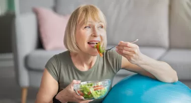 Senior woman eating healthy food against an exercise ball.
