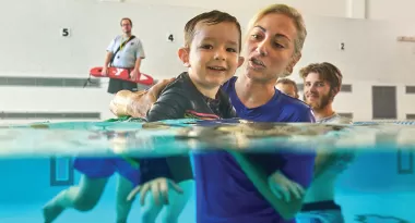 A toddler smiles as he learns to swim in a ymca parent and child swimming lesson.