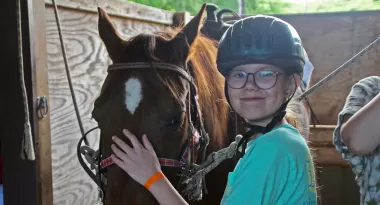 a girl in a green shirt and helmet with her horse in the stable