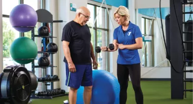 an older man is instructed on proper form by a ymca personal trainer