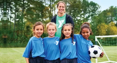 a ymca youth soccer volunteer coach smiles with her girls youth soccer team