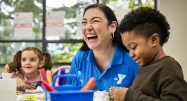 A YMCA Staff member and children laugh during a craft project in Child Watch