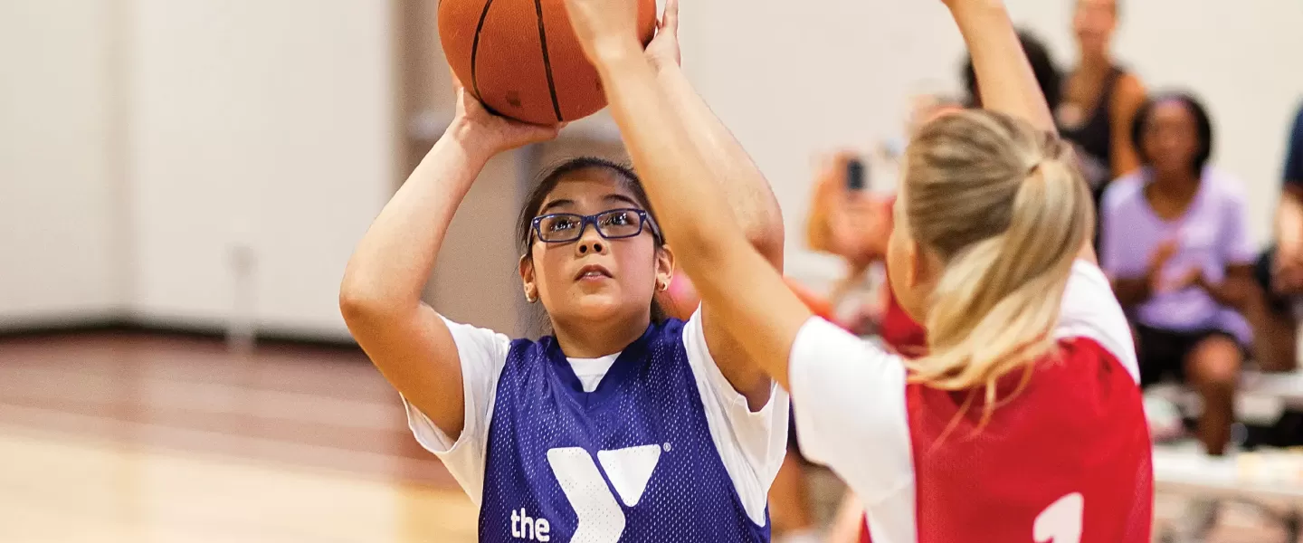 A young YMCA sports participant shoots a basketball goal during a YMCA Youth Basketball game