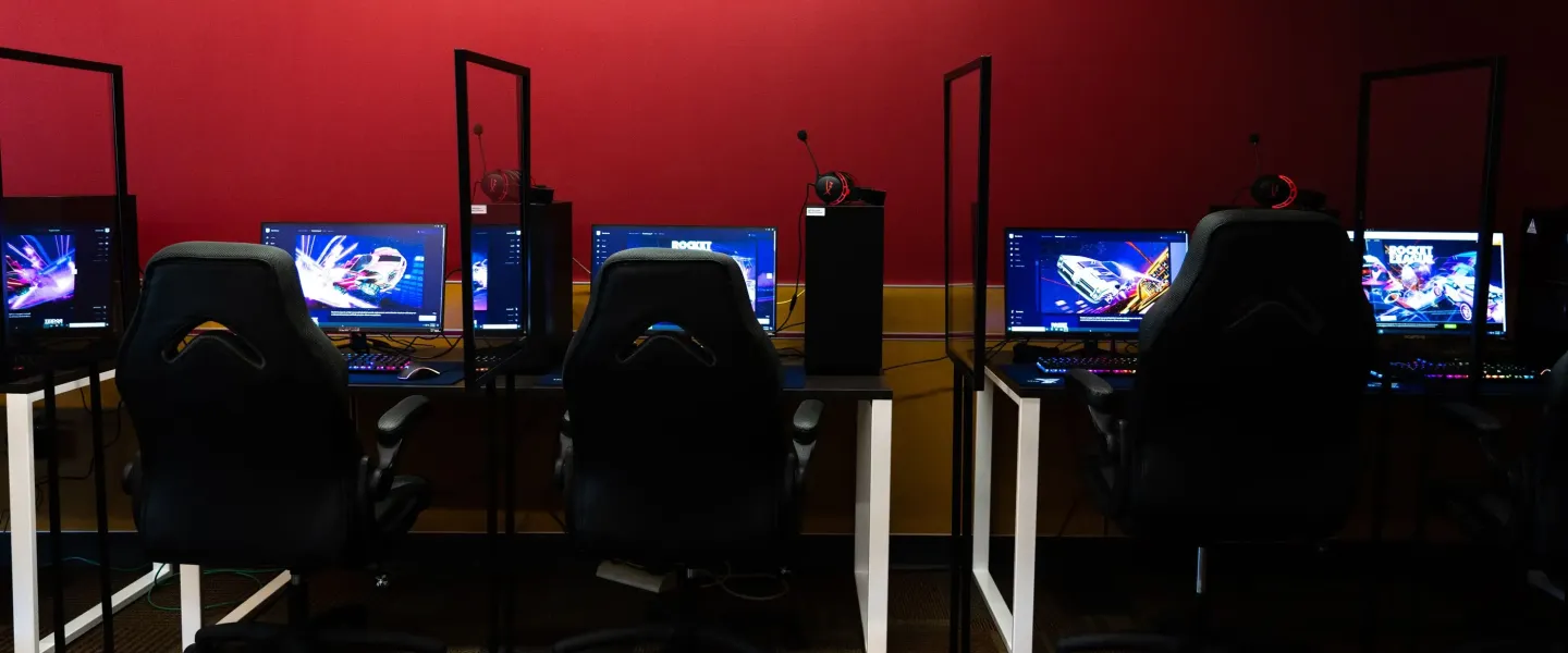An image of the computers in the esports arena at the YMCA against a red wall.