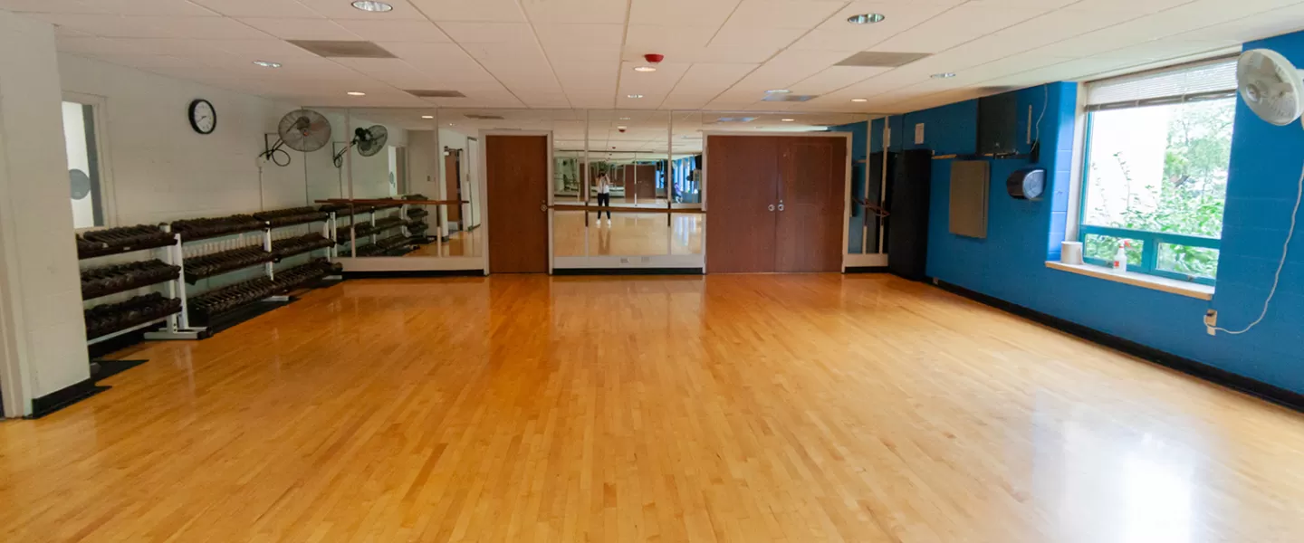 Group exercise studio with free weights organized on side. Yoga mats hung on wall.