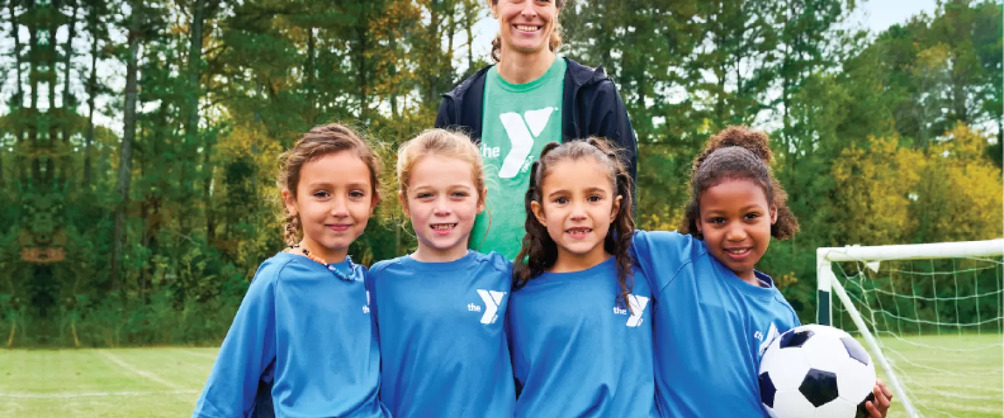 a ymca youth soccer volunteer coach smiles with her girls youth soccer team