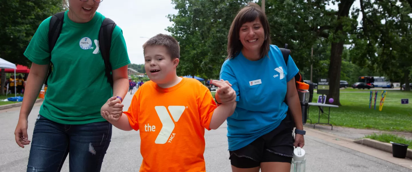 Two camp counselors holding hands with child as they walk down the street