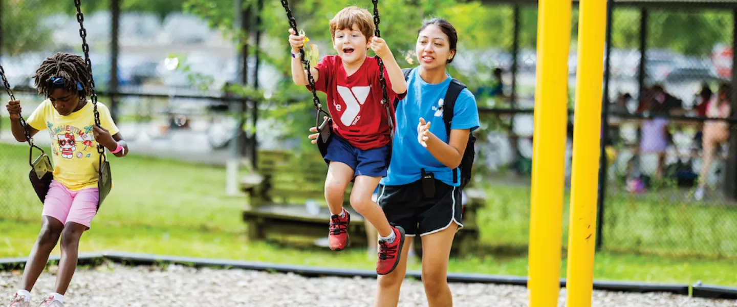 ymca camp counselor pushing campers on a swing