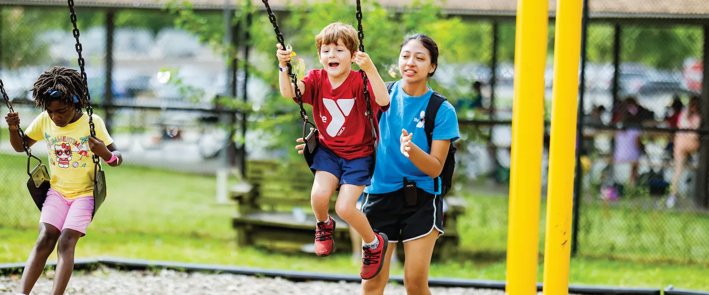 ymca camp counselor pushing child on swing