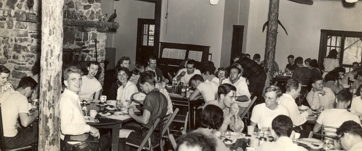 Guests in 1960s attire enjoying a meal together at long tables in the new lakefront dining hall at Trout Lodge.