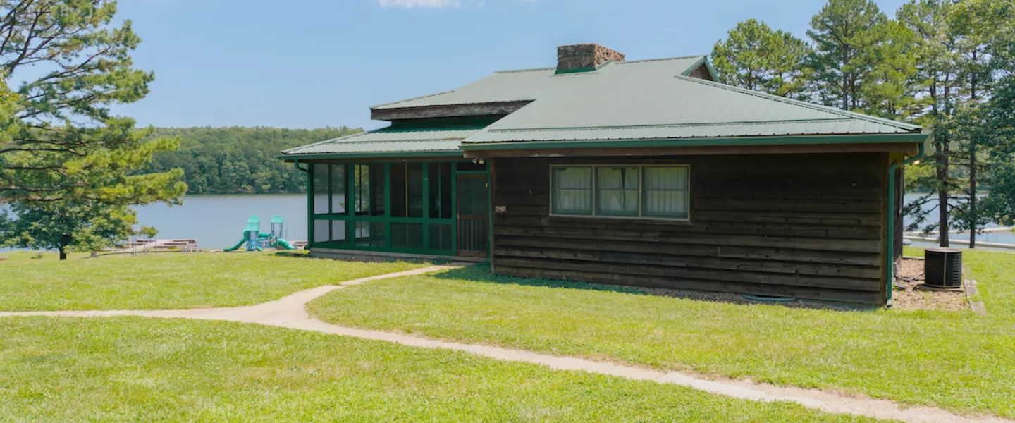 Exterior photo of a Lake View Cabin at YMCA Trout Lodge showing the screened-in porch, views of Sunnen Lake, and a nearby playground for families and kids