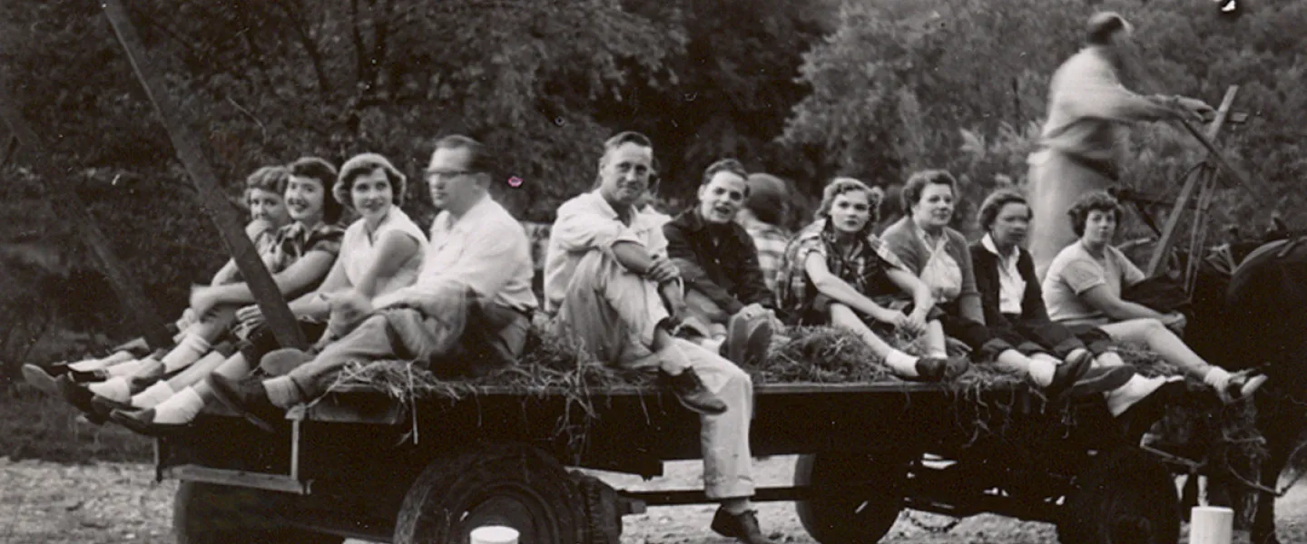 A group of smiling guests, including children and adults, sitting on hay bales during a tractor-pulled hayride.