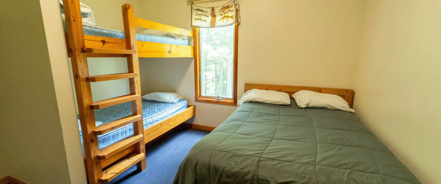 A Trout Lodge Forest View Cabin bedroom with a queen bed and two twin-size bunk beds with linens provided.