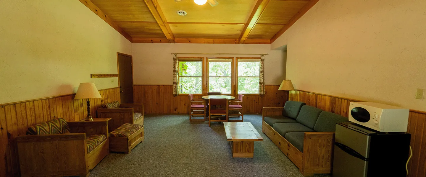A view of a Forest View Cabin living space area that includes a table and chairs, several couches and seating areas, mini fridge, microwave, and vaulted beam ceilings.