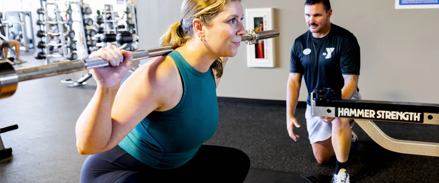 A certified YMCA Personal Trainer assists a ymca member with a deadlift squat with a plate weight bar.