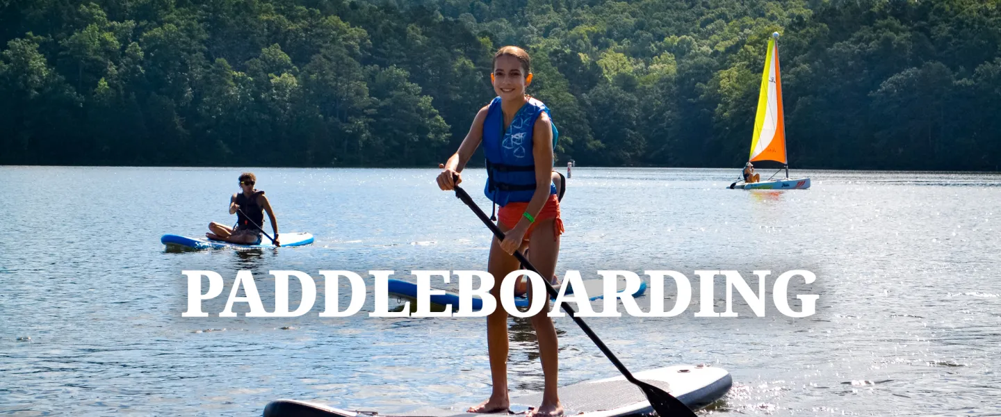 A camper balancing while standing up and paddling on a paddleboard on Sunnen Lake.