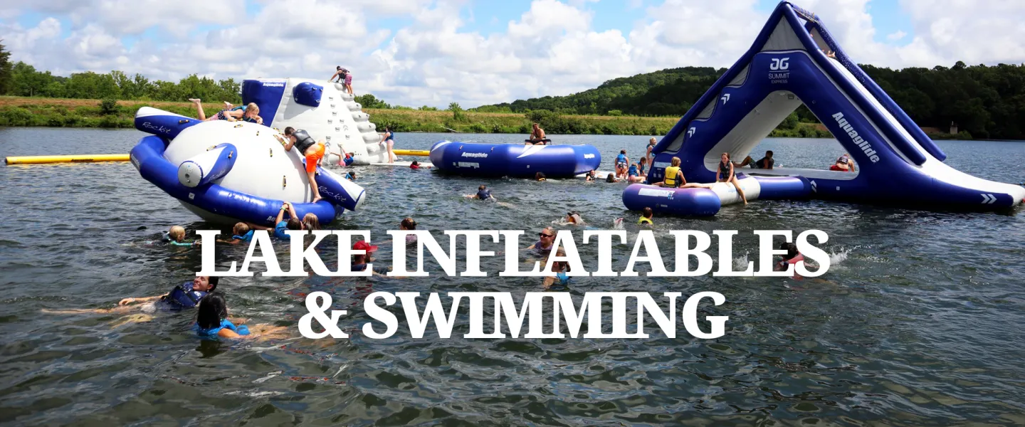 Campers wearing life jackets climbing and sliding on the large inflatable obstacle course on Lake Sunnen.
