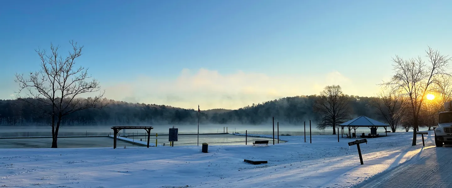 Panoramic view of frozen Sunnen Lake with the sun setting behind the snow-covered Ozark hills at YMCA Trout Lodge.