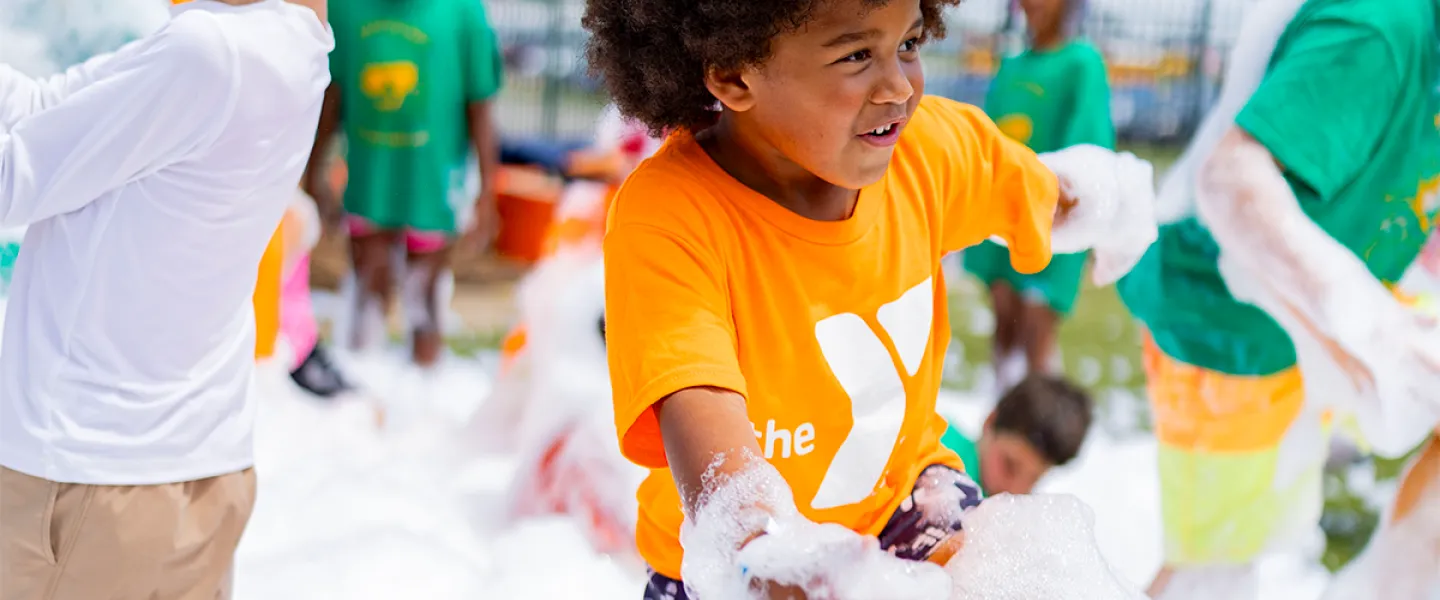 YMCA Summer Day Camp participant on a field trip having fun in a sea of foam bubbles at a ballpark bubble party