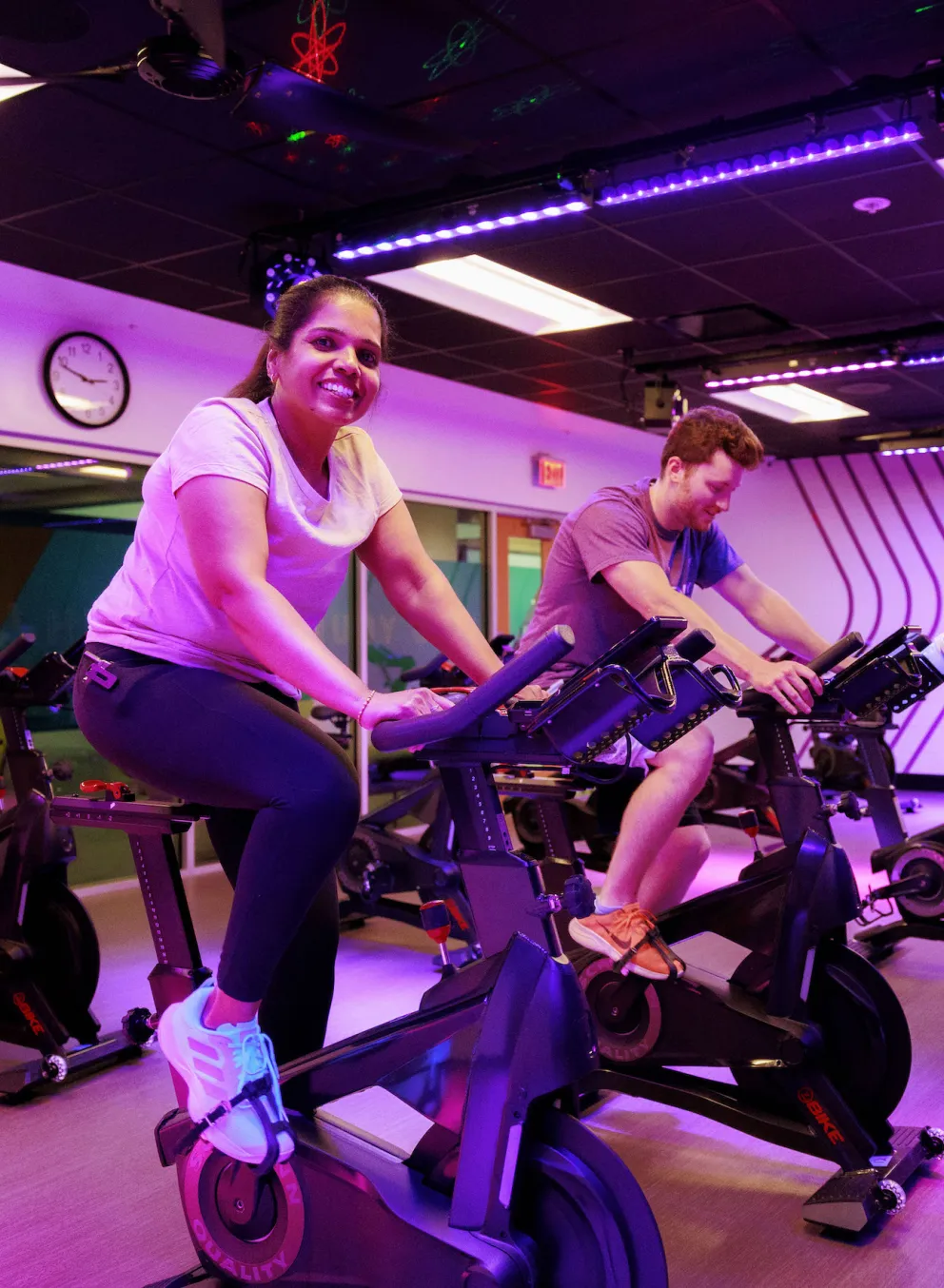 A woman smiling at the camera while exercising on a spinning bike inside of the Chesterfield YMCA's cycling studio during a group exercise class