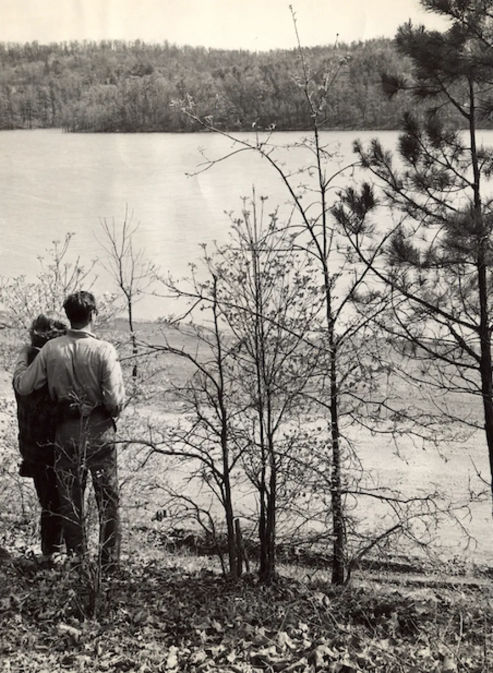 Historical photo of Sunnen Lake at YMCA Trout Lodge in Potosi, MO with a couple and their dog standing by the lake gazing out at the water and beautiful Ozark's mountain scenery