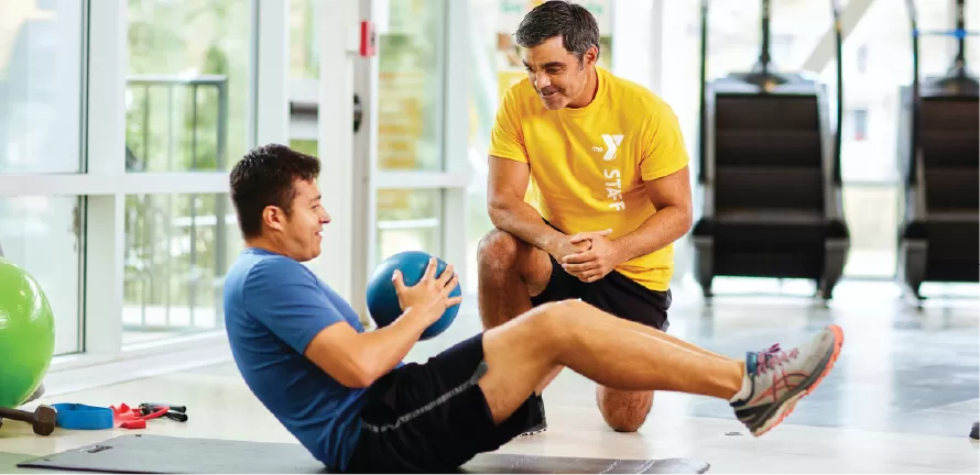A YMCA Personal Trainer guides a Y member through an ab workout using a medicine ball.
