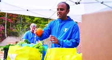 A man places an orange into a ymca grocery bag.
