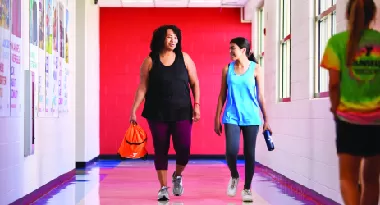 Two women walk down the hall of a ymca talking