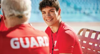A ymca lifeguard sitting by an outdoor pool smiling