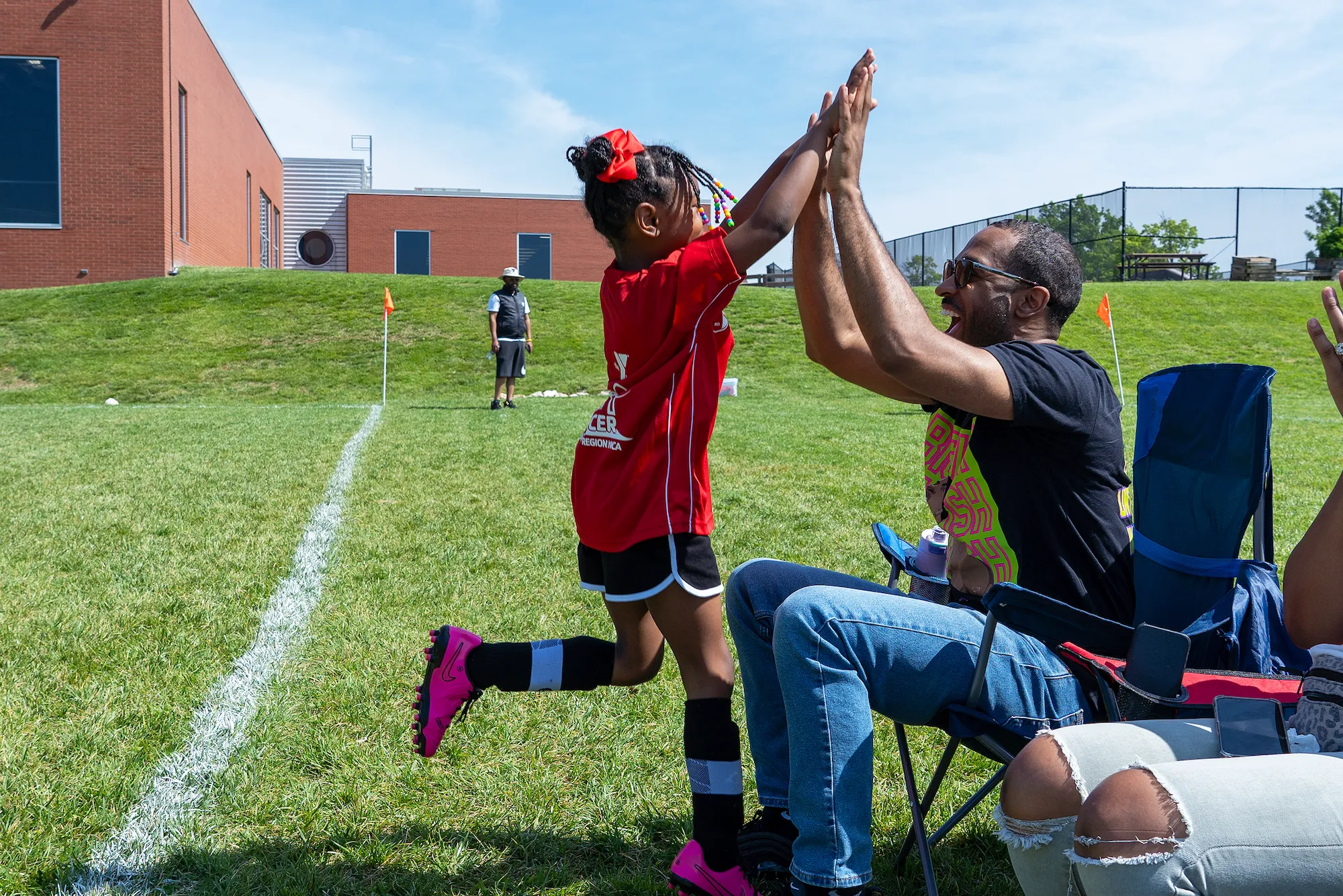 A young girl at the CITY SC Kickoff event high-fives her father on the sidelines as he cheers her on during the youth soccer game.