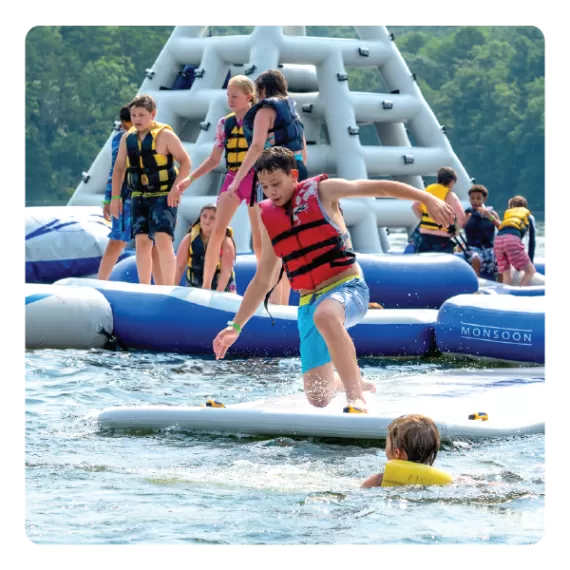 A boy jumps into the lake off of the inflatable water park at ymca camp Lakewood