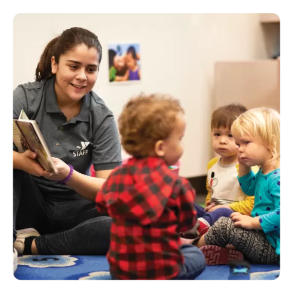 a ymca early childhood education staff member reads to three infants