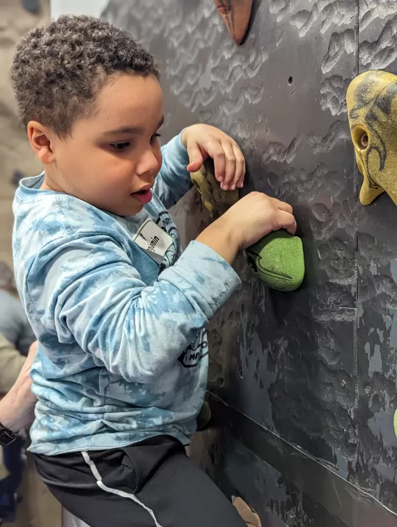 young boy climbing a rock wall at the south county ymca