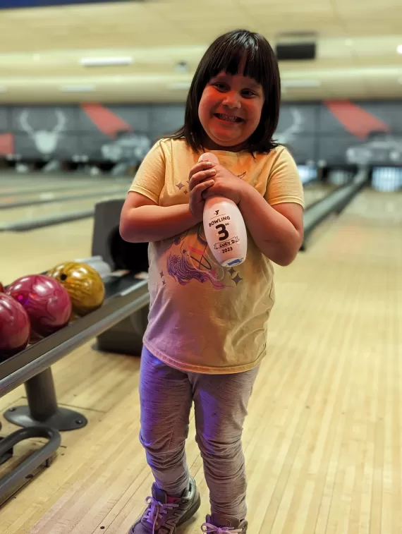 young girl holding bowling pin in bowling alley for ymca adaptive sports