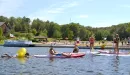 Thumbnail: A group of male and female teens enjoy the lake and water-based activities during a program at Trout Lodge YMCA. The students are doing a variety of activities like kayaking, paddle-boarding, and swimming in inflatable floaties. All teenagers look to be having a fun experience.