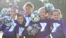 Thumbnail: An image of five young girls from a cheer team at the Four Rivers YMCA. The girls have on purple YMCA t-shirts and are holding silver pom-poms.