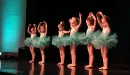 Thumbnail: Six young Caucasian female ballerinas pose in fifth position in their green leotards and tutus as they perform their recital from their local dance and ballet program at the YMCA.