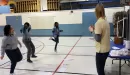 Thumbnail: An image of a Caucasian after school leader playing a game where the three African American children in her care are captured jumping on one foot, smiling.