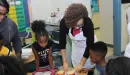 Thumbnail: Two African American females in their middle ages helping a classroom of kids with nutrition skills. The instructor on the right is wearing a white apron over her clothes.